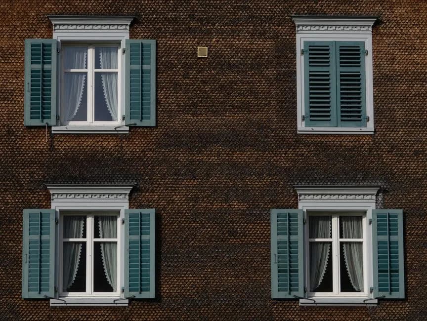Close-up of a brown building exterior featuring green window shutters and curtains.