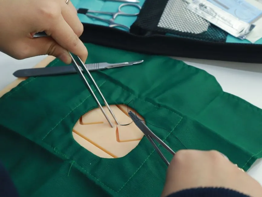 Close-up of hands practicing suturing on a medical simulator with tools.