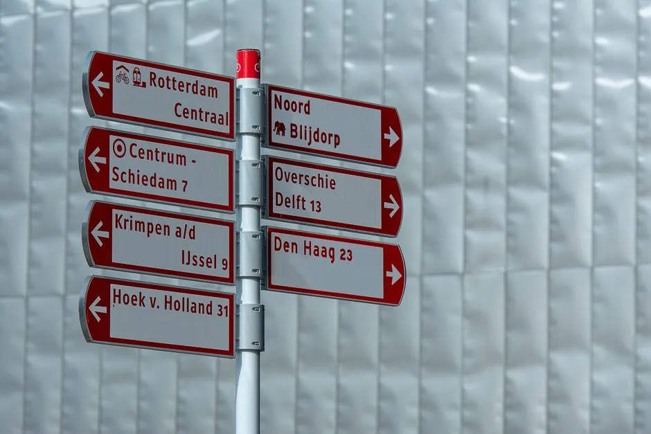 Directional signpost in Rotterdam with various city destinations, including Den Haag and Delft.