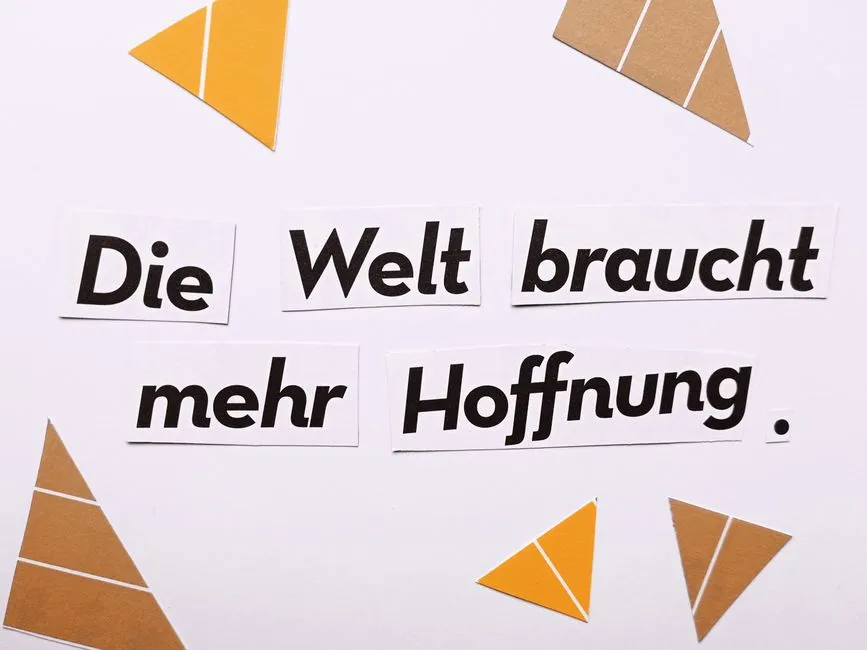 Inspirational text 'Die Welt braucht mehr Hoffnung' on a white background with triangle cutouts.