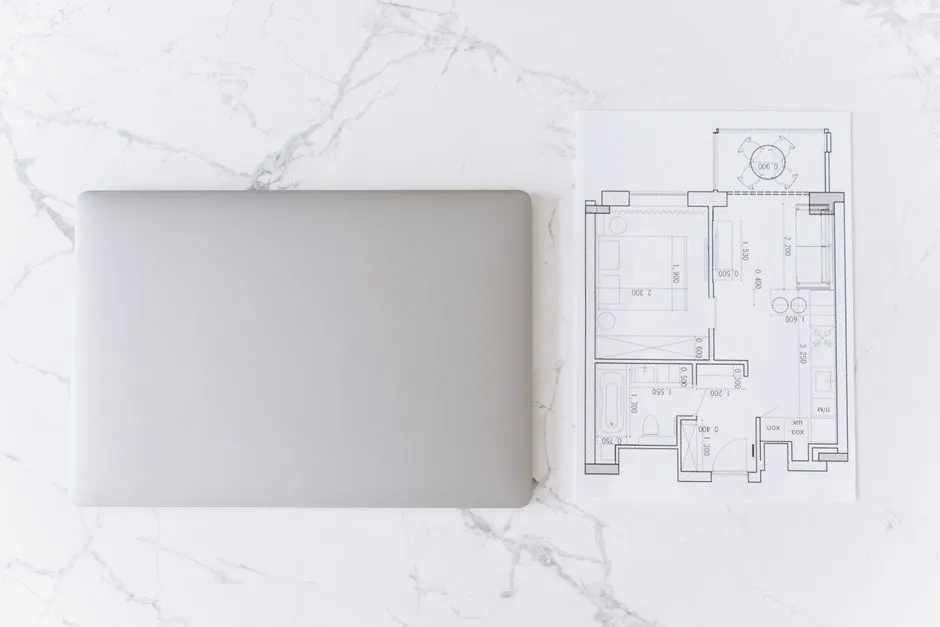 Top view of a laptop and architectural blueprint on white marble surface, showcasing modern workspace.