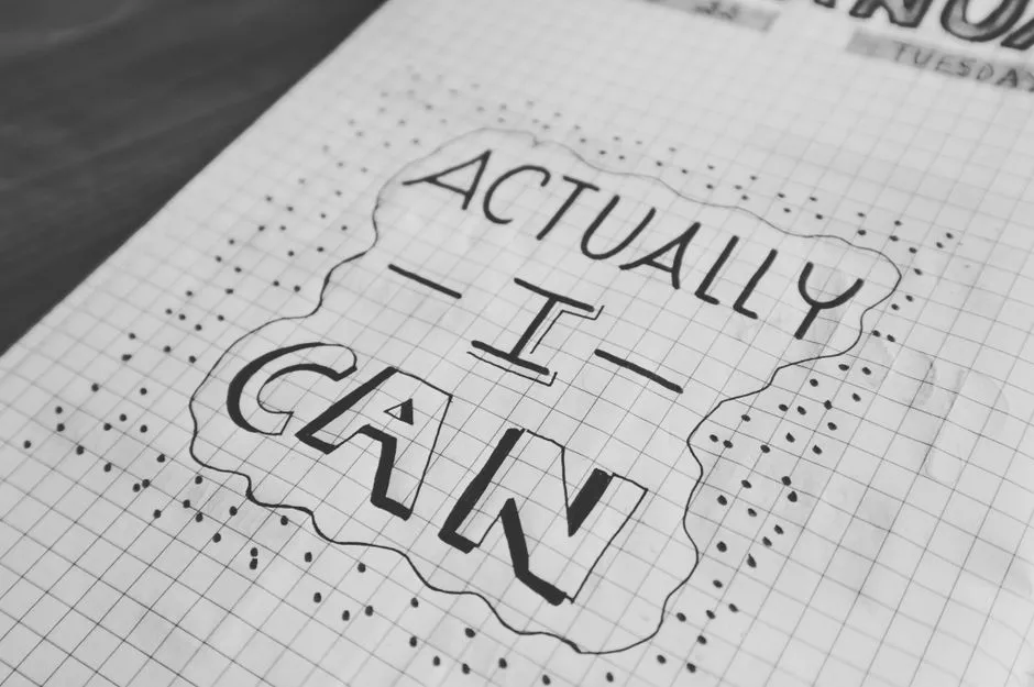 Motivational text 'Actually I Can' on a grid paper background. Black and white close-up.