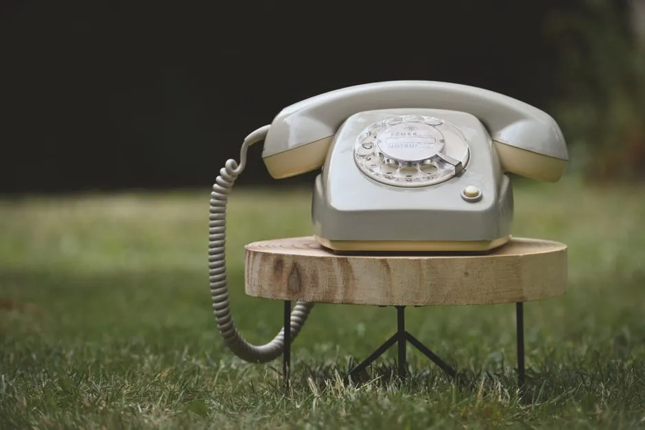 A classic rotary telephone sits on a wooden table in an outdoor setting, evoking nostalgia.