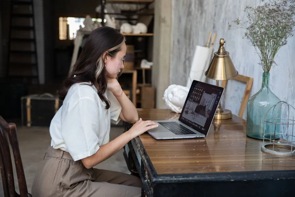 Focused young woman working on a laptop at a rustic desk, embodying modern remote work culture.