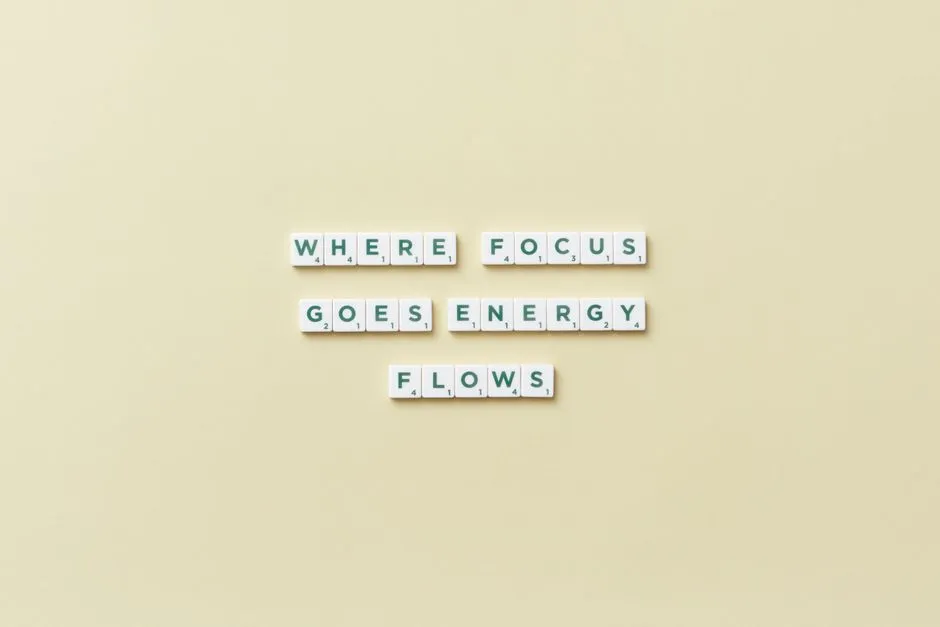 Inspirational quote 'Where Focus Goes Energy Flows' spelled with Scrabble tiles on a minimalist background.