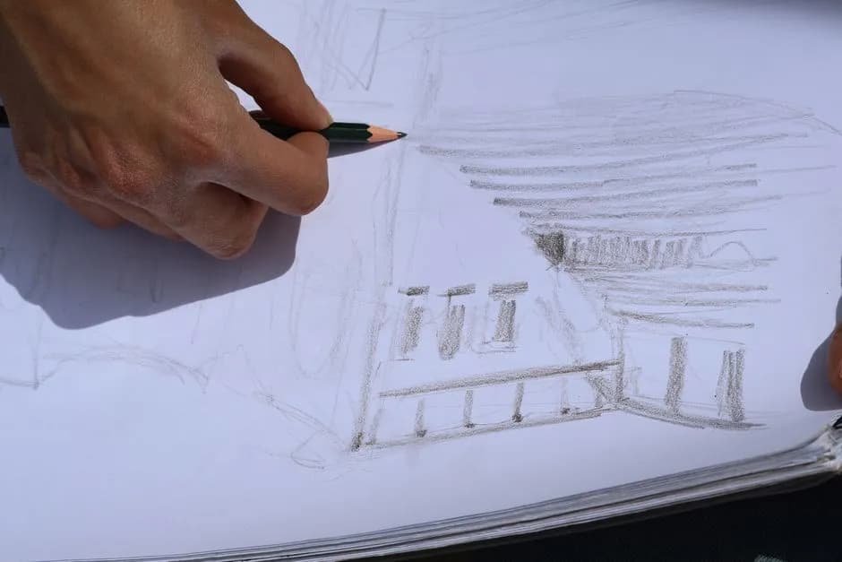 Artist sketching a building in a sketchbook outdoors, showcasing urban architecture.
