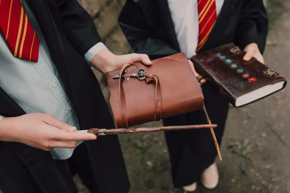 Two children in wizard costumes holding a wand and spell book outdoors, resembling magic school theme.