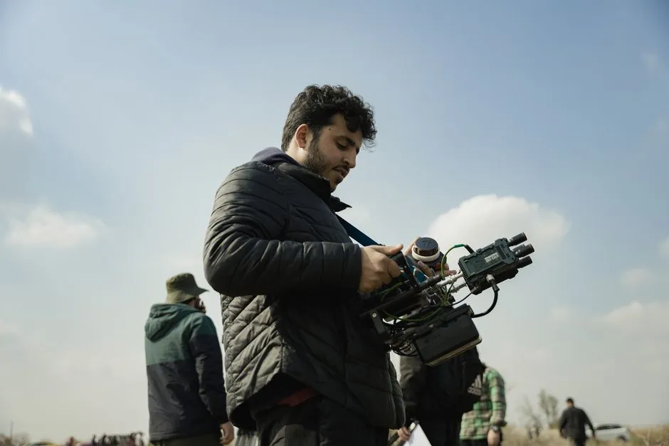 Videographer sets up camera rig outdoors with clear sky and casual attire, capturing scenic shots.