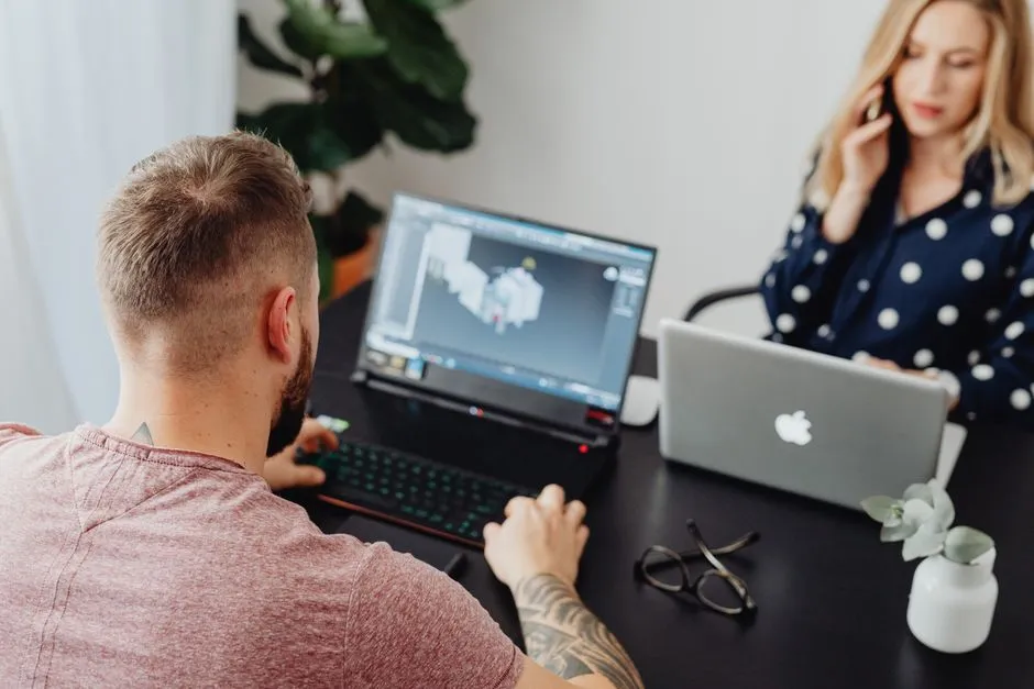 Two professionals working on laptops, engaging in a collaborative office environment.