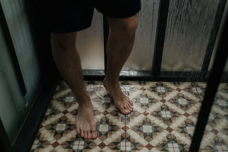 Close-up view of a person standing with wet feet on a tiled shower floor.