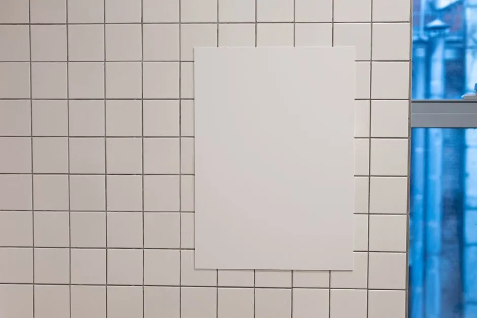 Blank white placard hanging on wall covered with white tiles inside of building