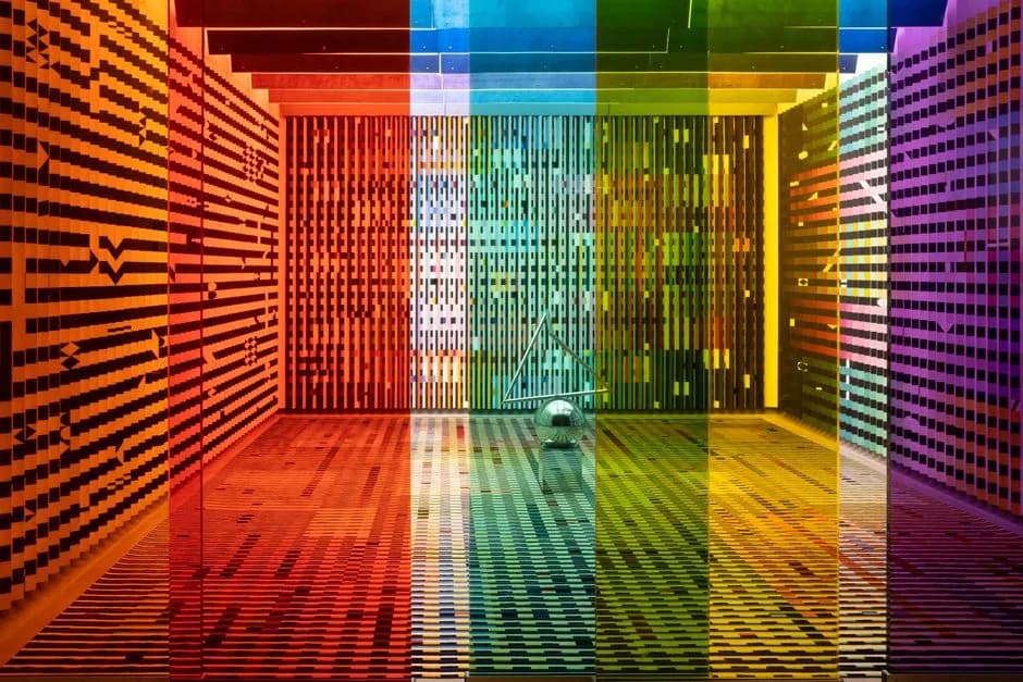 A vibrant, rainbow-themed room featuring patterned walls and colored glass panels creating a kaleidoscopic effect.