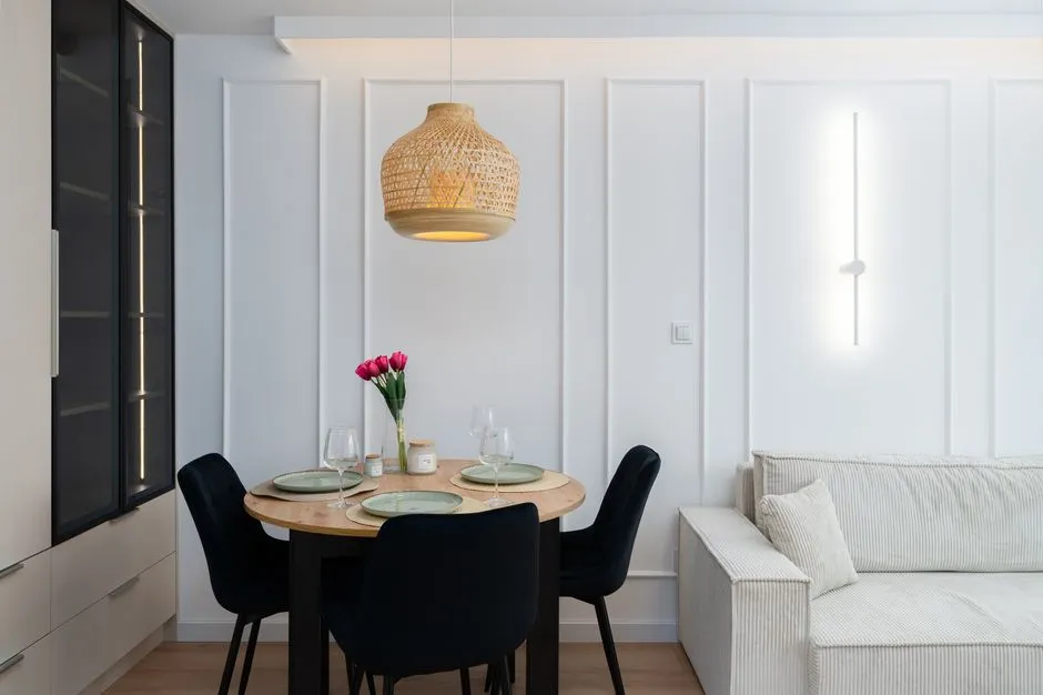 Bright dining area in Kraków, featuring a wooden table, wicker lamp, and minimalist design.