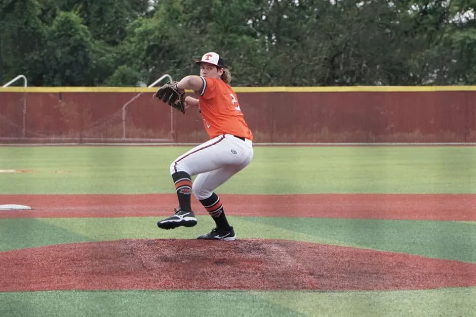 A baseball player in orange jersey pitching on a sunny day.
