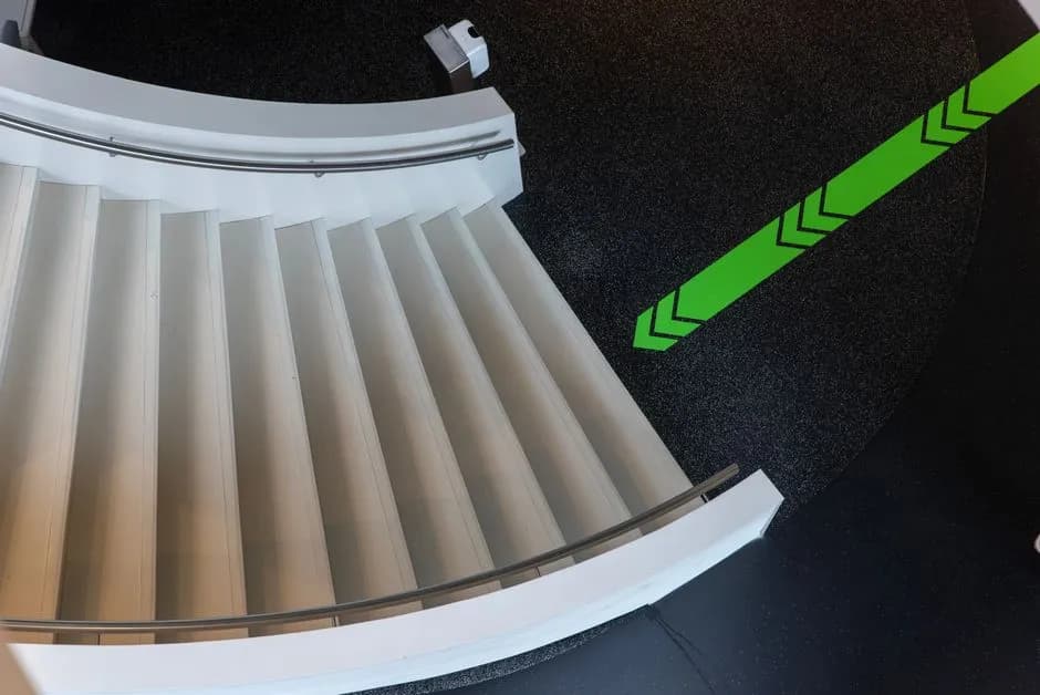 Top view of a modern curved staircase with a green directional arrow on the floor.