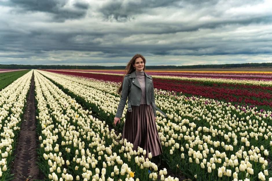 A woman walks through a colorful tulip field under a dramatic cloudy sky.