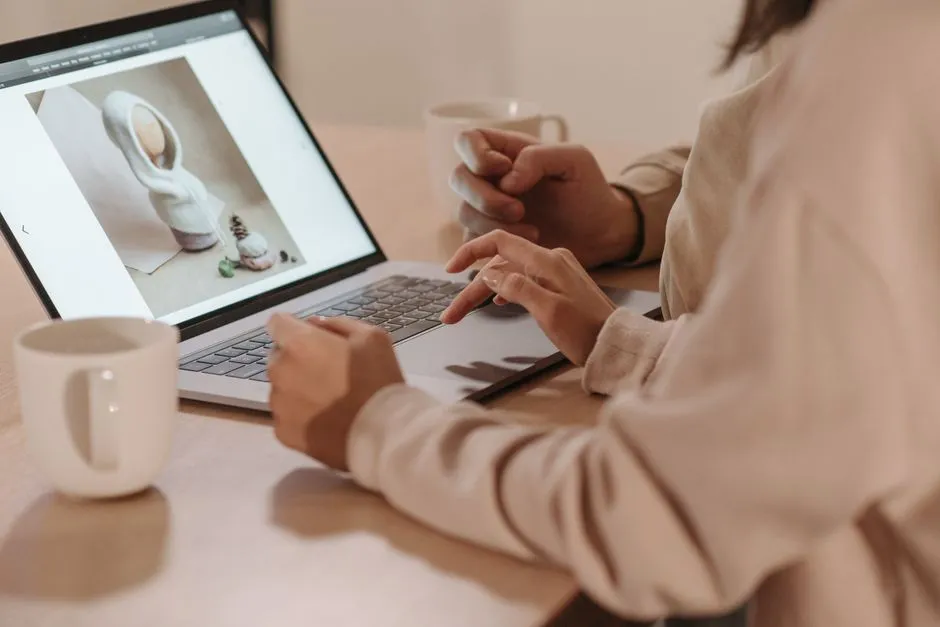 Two individuals reviewing a photo on a laptop, enjoying coffee indoors.