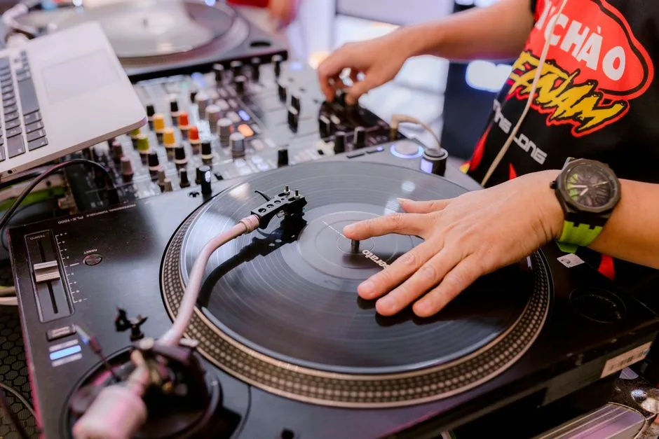 Hands of a DJ playing vinyl on turntables at an indoor music event.