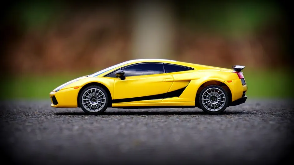 Close-up of a yellow toy car resembling a sports car model on asphalt with blurred background.