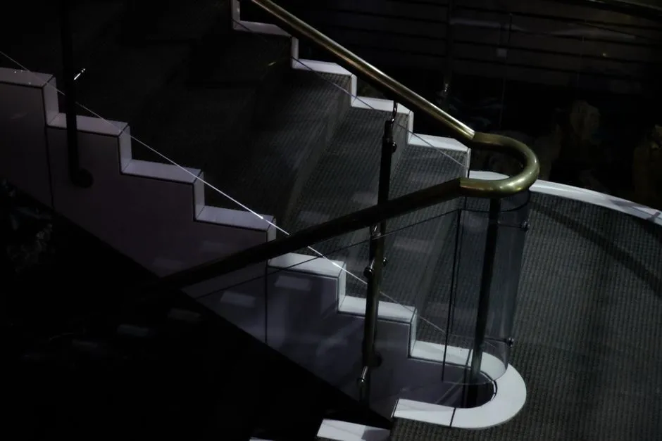 A sleek and modern glass staircase with a metal handrail in a dimly lit environment.