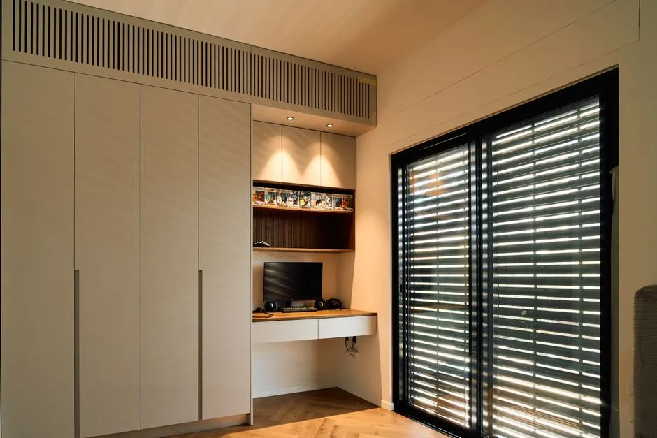 A minimalist home office with sleek design and ample natural lighting through large blinds.
