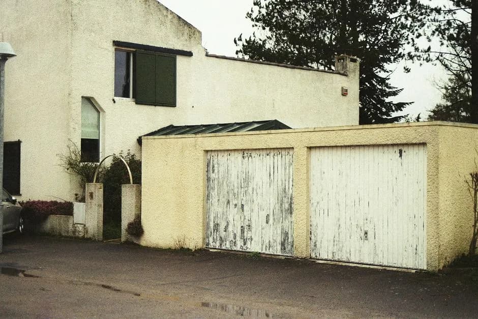 An old residential house with weathered garage doors in an urban setting.