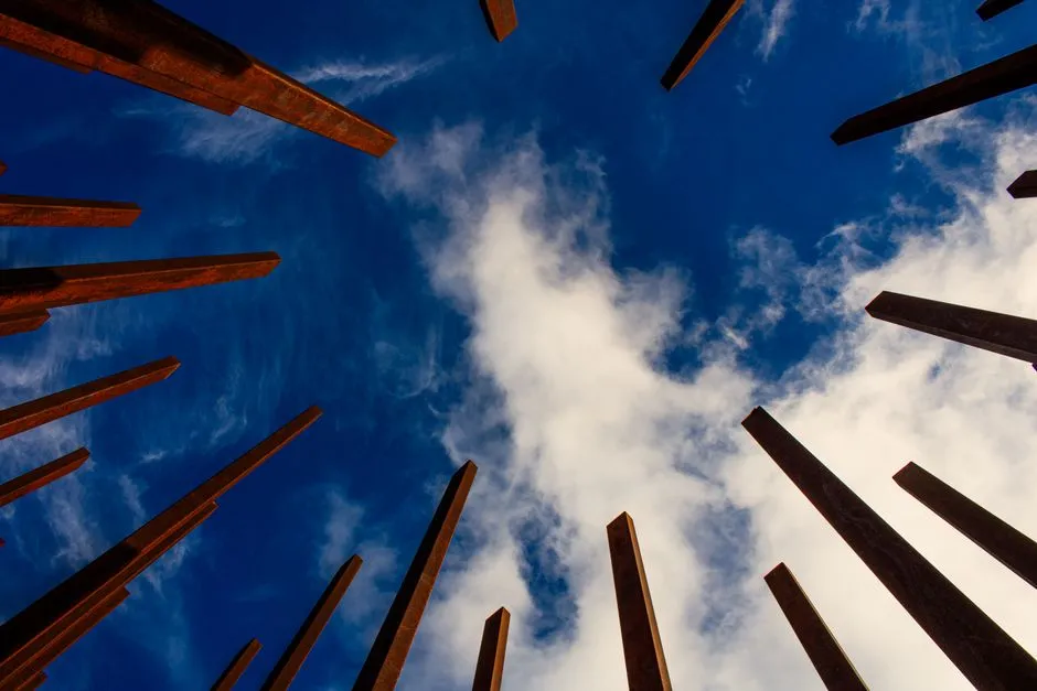 View of sky through abstract vertical metal beams creating a dynamic visual composition.