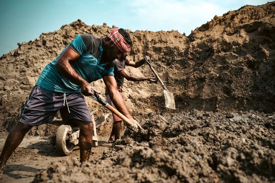 Two workers engaged in intensive digging at a construction site under blue skies.
