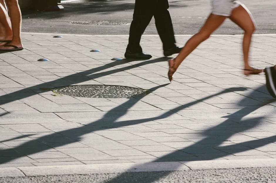 Pedestrians casting long shadows on a sunny city street, capturing urban movement and lifestyle.