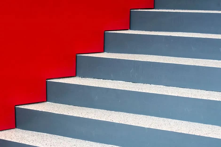Image of a modern staircase against a vibrant red wall, highlighting geometric design and contrast.