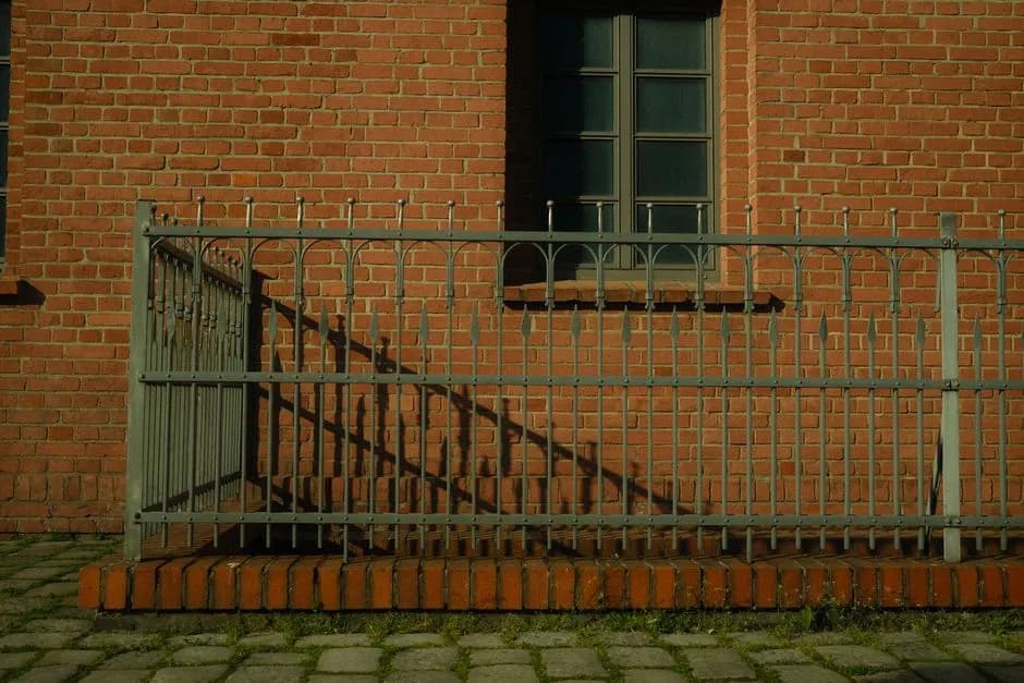 Close-up of a brick wall with decorative metal railings casting shadows in daylight.