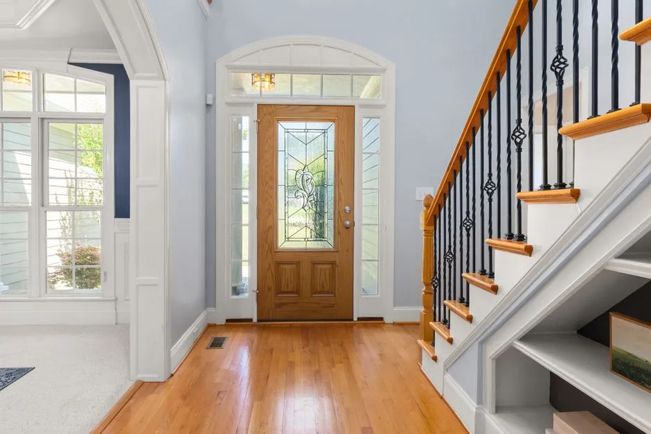 Bright and airy home entrance featuring a wooden door, glass panels, and elegant staircase.