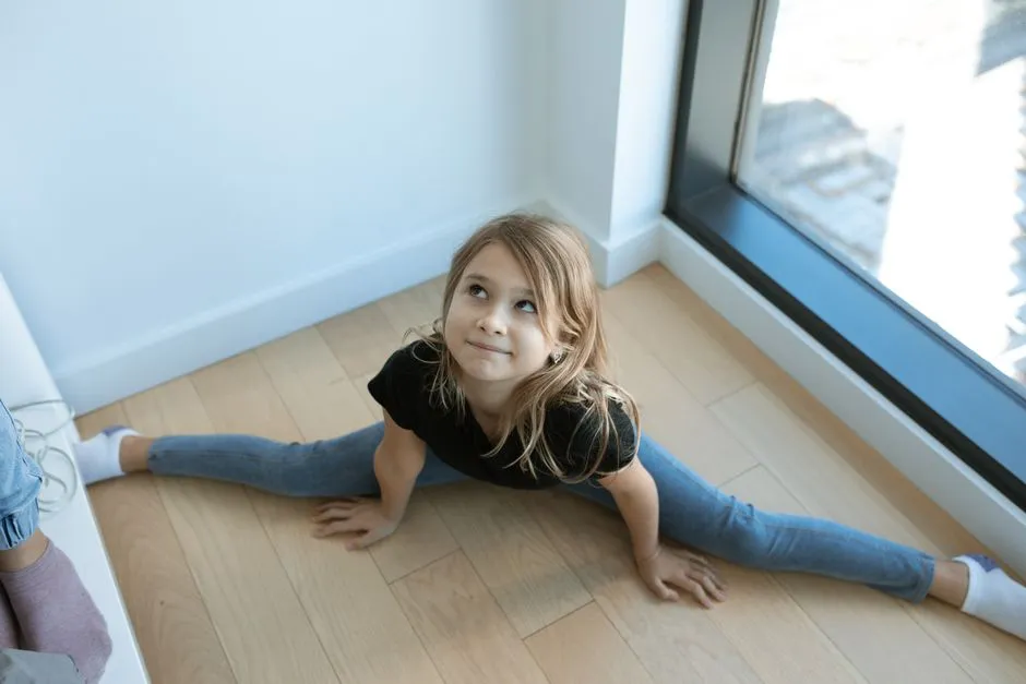 Young girl performing a split on wooden floor, showcasing flexibility and concentration indoors.