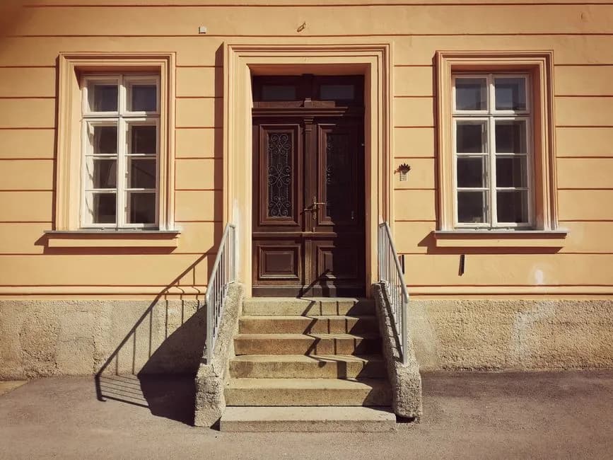 A classic entryway featuring wooden double doors and a stone staircase, framed by large windows.