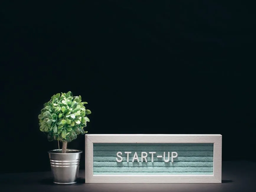 A modern close-up of a start-up theme with a potted plant and text board on a black background.