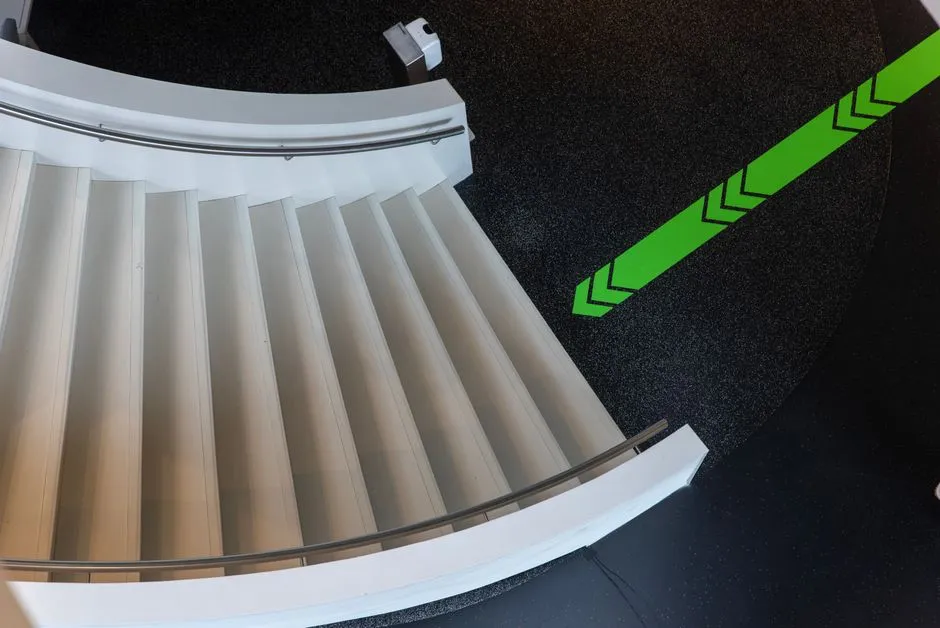 Top view of a modern curved staircase with a green directional arrow on the floor.